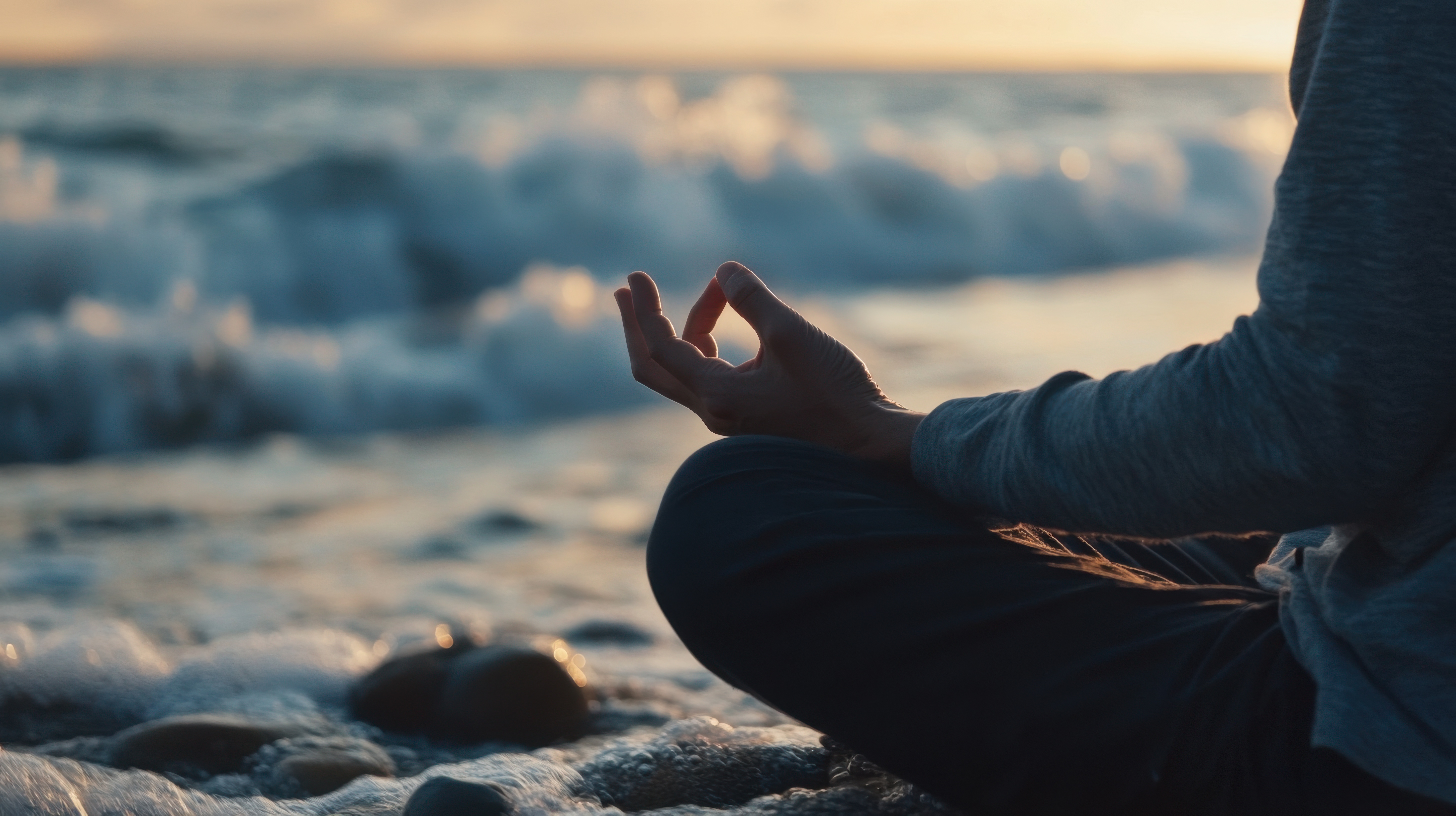 Person meditating on a beach at sunset — peaceful ocean waves and warm golden light